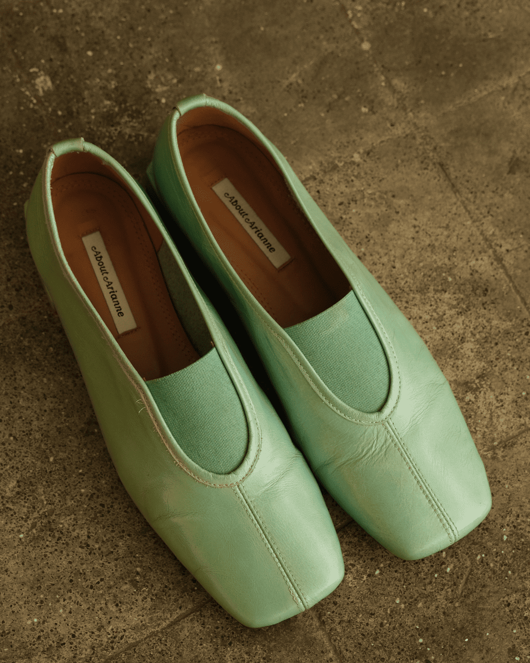 A pair of mint green leather slip-on shoes with a square toe, displayed on a textured concrete surface. The brand name 'JACKIE CAUSSEAU' is visible on the insole labels.