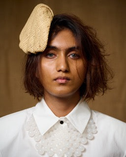 A woman wearing a beige cane clip-on hat shaped like a shell, paired with a white shirt and a necklace. 
Andrea Viêntëc - Cane Hat - sold by two extra lives 