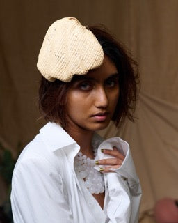 A woman wearing a beige cane clip-on hat shaped like a shell, paired with a white shirt and a necklace. 
Andrea Viêntëc - Cane Hat - sold by two extra lives 