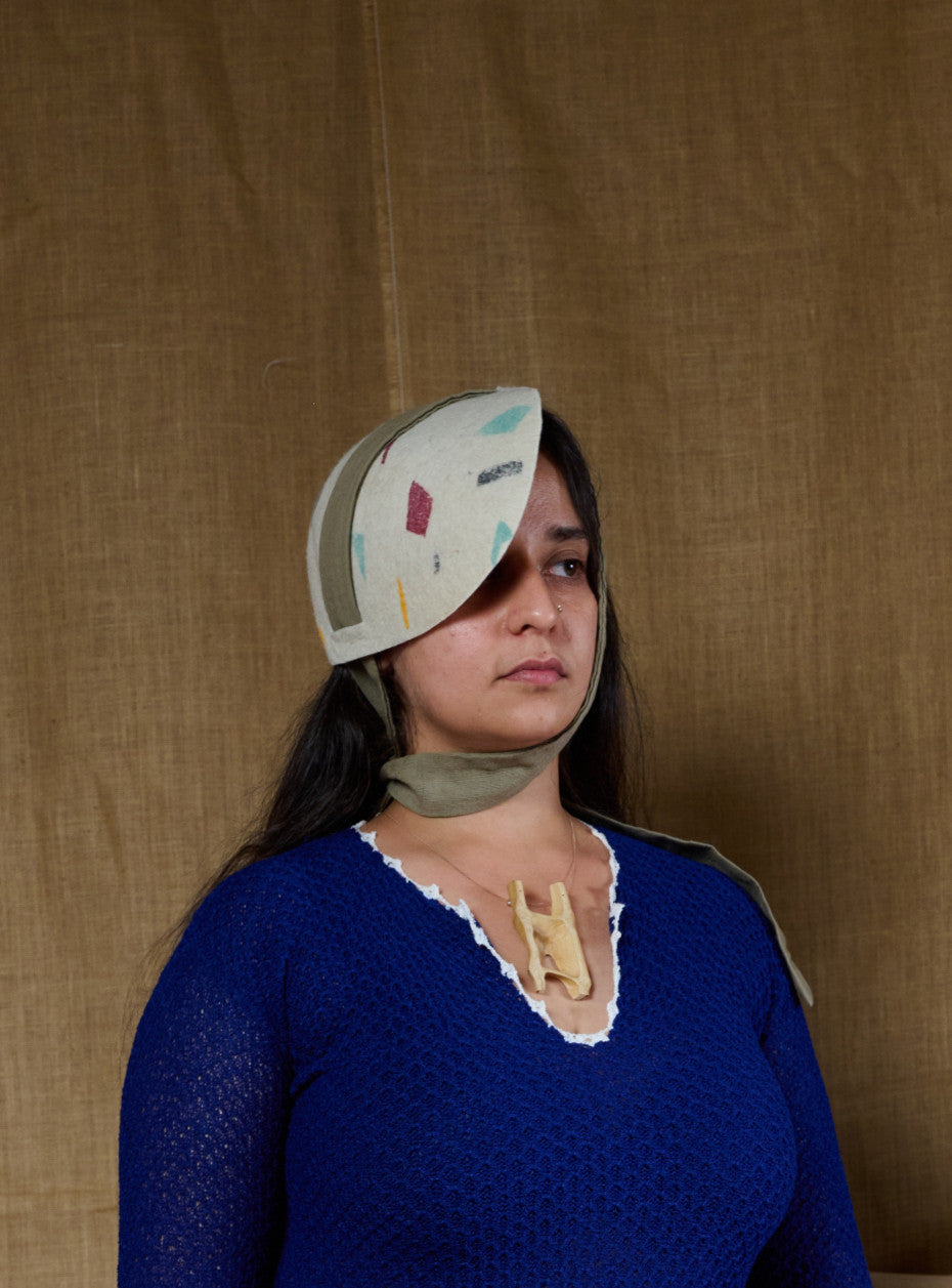 A woman wearing an off-white tieable hat with a geometric pattern, standing against a textured background. Andrea Viêntëc - Off-White Tieable Hat sold by two extra lives 