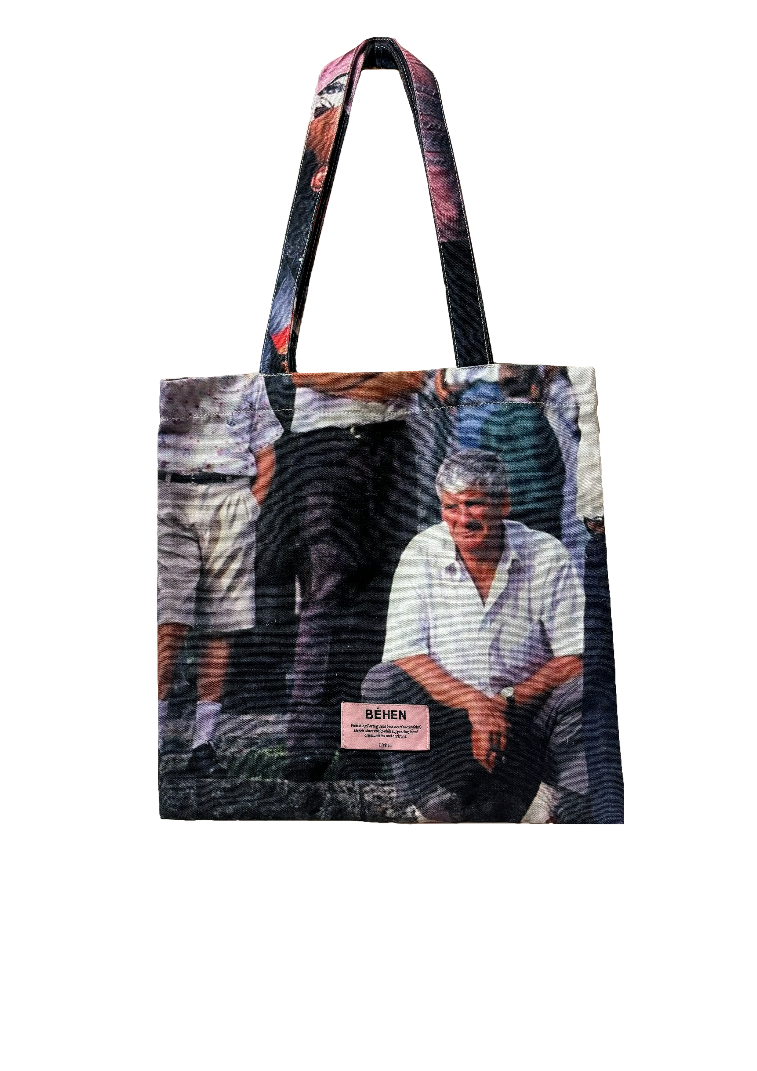 A tote bag featuring a black and white photograph of a man seated, with a pink detail on the bottom right side. Behen studio sold by two extra lives.