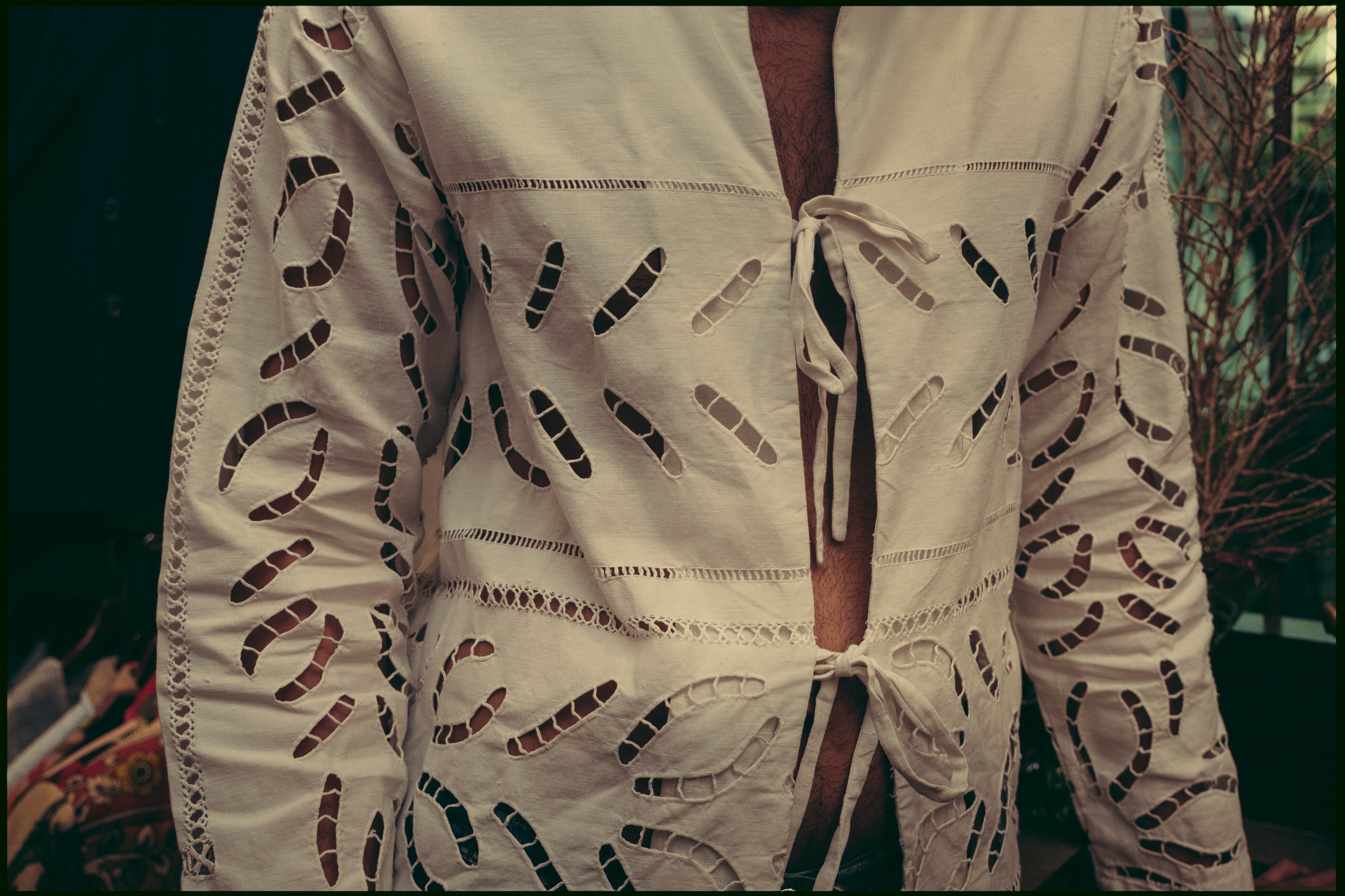 A person is wearing a white linen shirt with cutwork embroidery. The shirt has a collared neckline and short sleeves. Béhen - White Cutwork Shirt sold by two extra lives