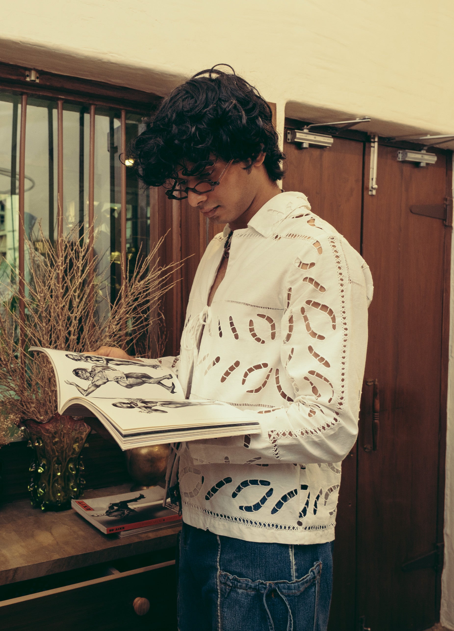 A person is reading a book while wearing a white linen shirt with cutwork embroidery. The shirt has a collared neckline and short sleeves. Béhen - White Cutwork Shirt sold by two extra lives