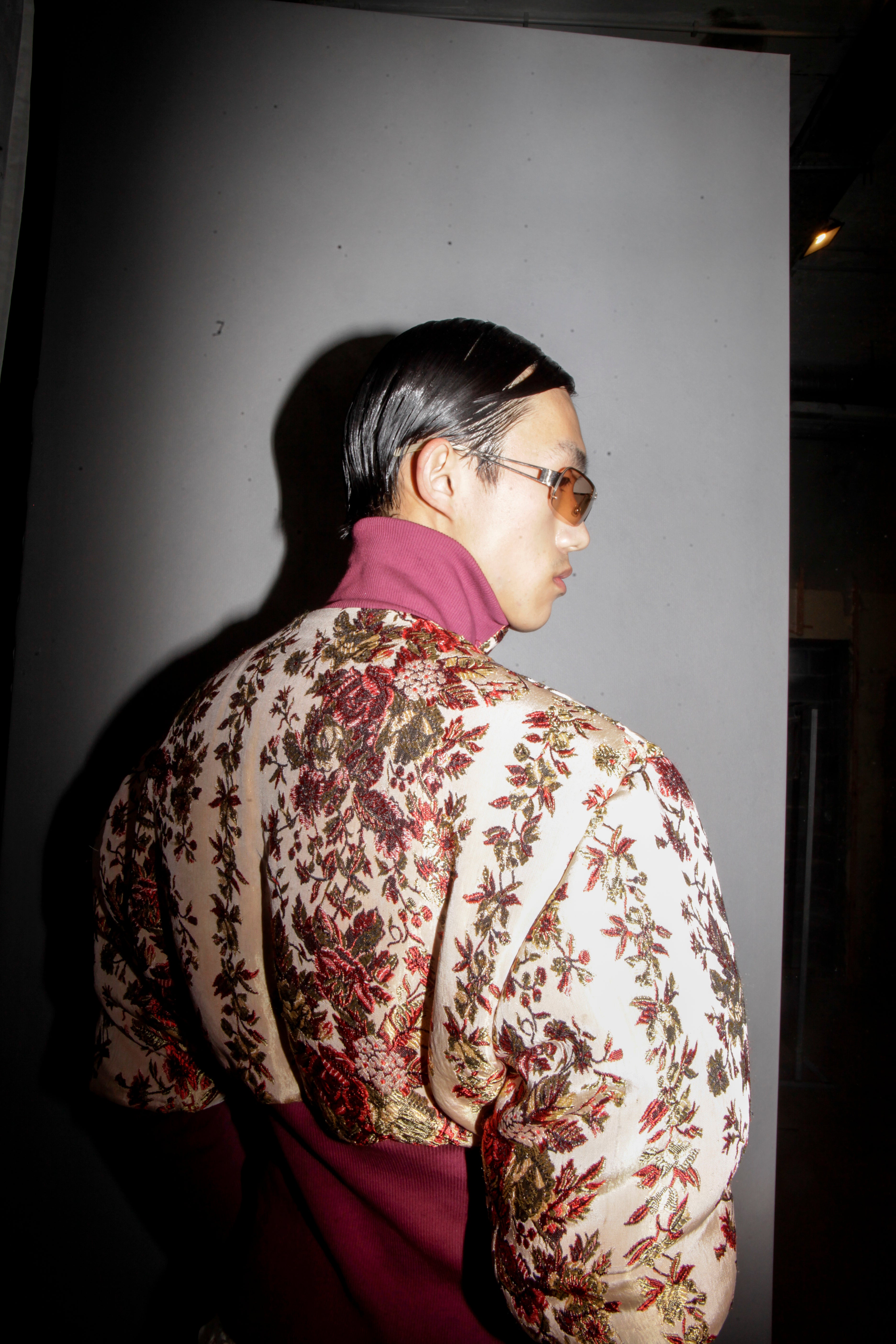 A person wearing a floral bomber jacket and sunglasses, standing in a casual pose with one hand on their hip. Béhen - Bed Cover Bomber sold by two extra lives.