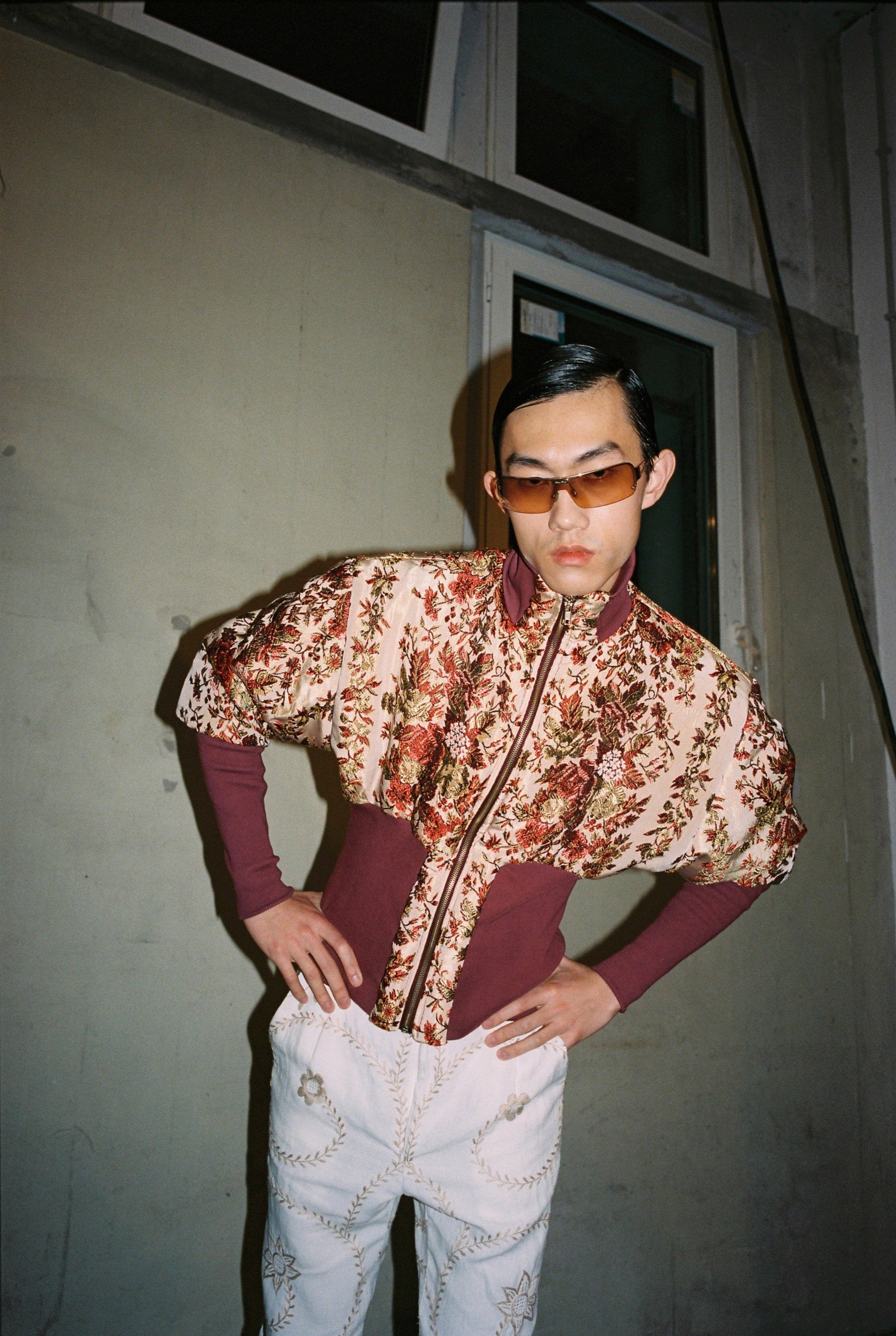 A person wearing a floral bomber jacket and sunglasses, standing in a casual pose with one hand on their hip. Béhen - Bed Cover Bomber sold by two extra lives.