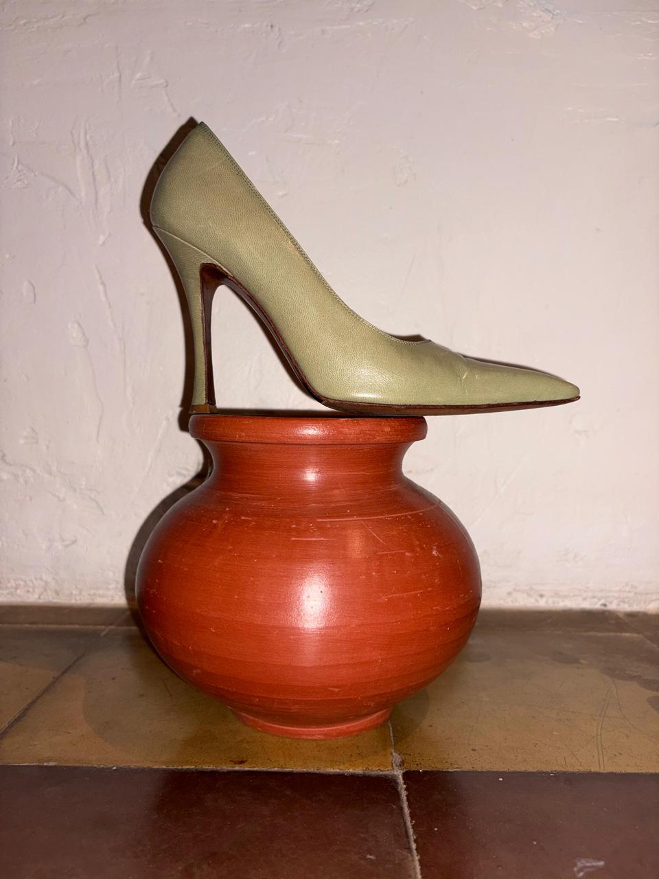 Green high-heeled shoe balanced on a red ceramic vase against a plain Green high-heeled shoes on a checkered floor with a red vase. Christian Dior - Vintage Sage Pumps sold by two extra liveswall.