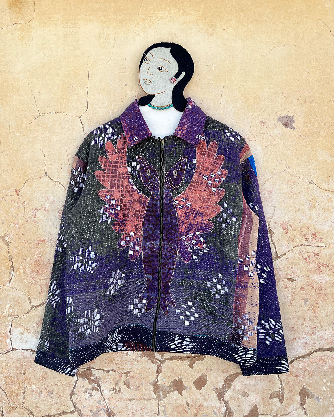 Textile art piece with a person wearing a patterned garment on a textured beige background DAY-AND-AGE-BHERUNDA-JACKET-TWO-EXTRA-LIVES