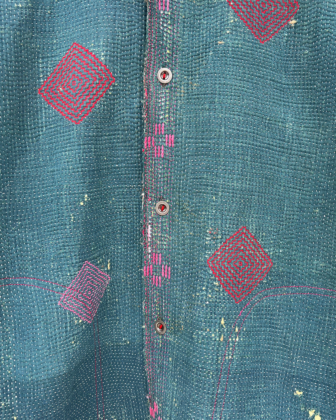Close-up of a teal fabric with pink geometric patterns and buttons. DAY-AND-AGE-TWILIGHT-JACKET-TWO-EXTRA-LIVES