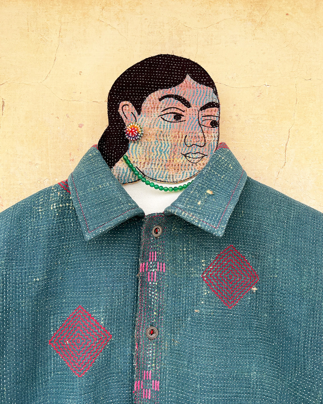Textile art piece with a person wearing a blue garment with geometric patterns on a beige background DAY-AND-AGE-TWILIGHT-JACKET-TWO-EXTRA-LIVES