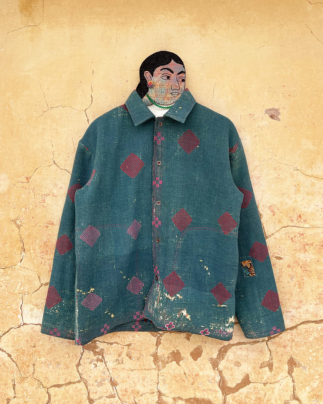 Teal jacket with red geometric patterns on a textured beige wall DAY-AND-AGE-TWILIGHT-JACKET-TWO-EXTRA-LIVES