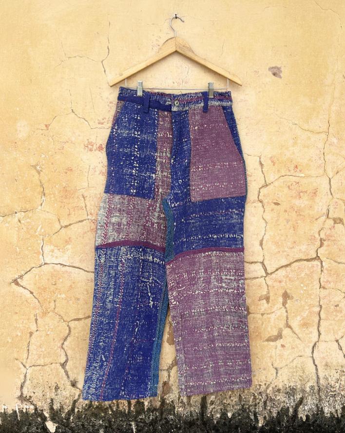 Pair of patchwork pants with kantha work by day and age hanging on a hanger against a textured beige wall. by two extra lives.