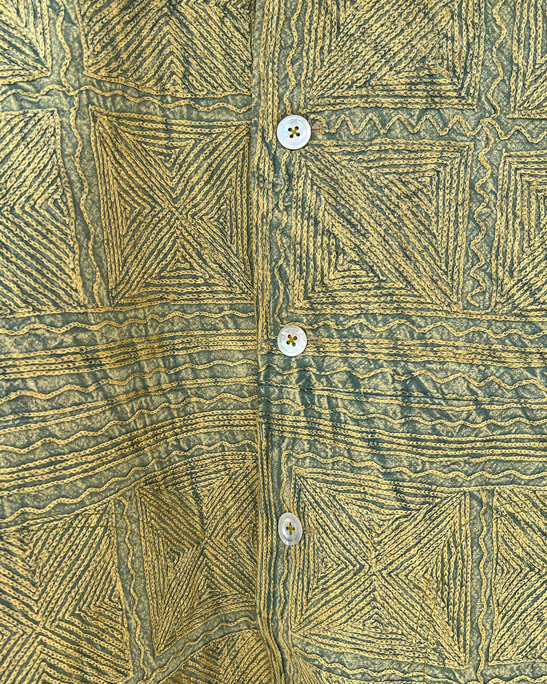 Green patterned jacket by day and age on a mannequin against a textured beige background, by two extra lives.