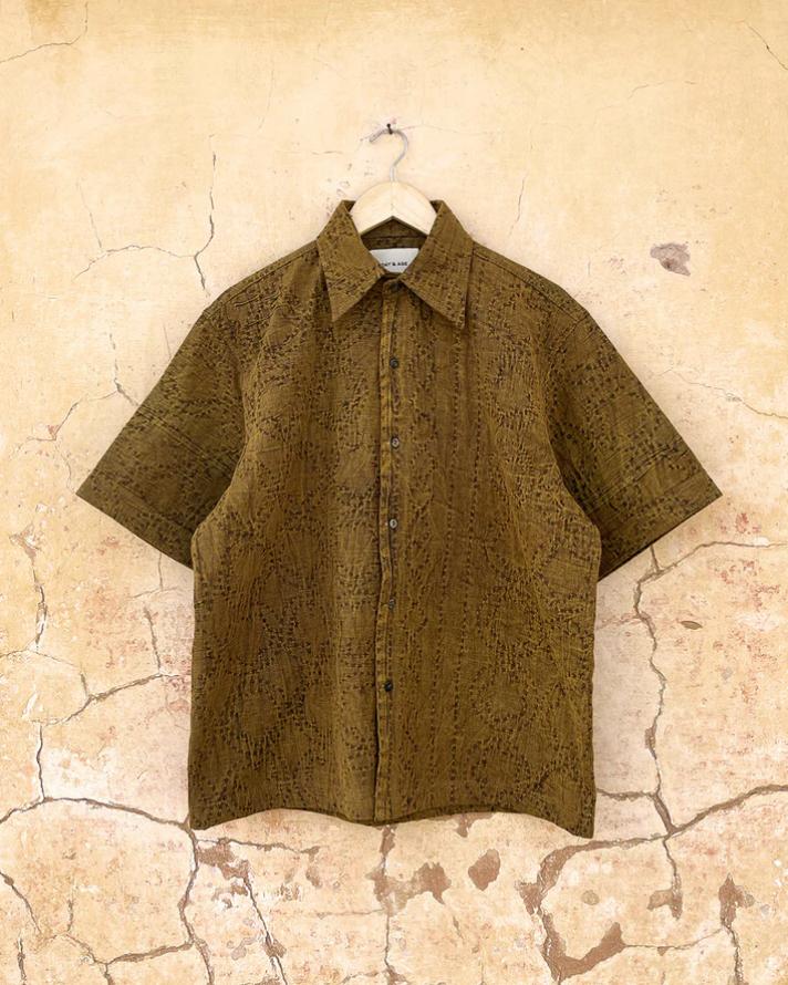Brown patterned shirt with kantha work by day and age on a hanger against a beige textured wall by two extra lives.