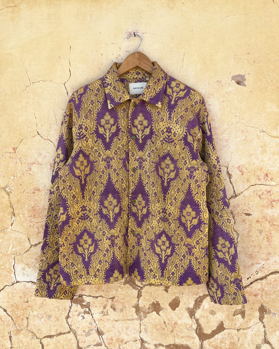 Patterned shirt jacket by day and age on a hanger against a textured wall by two extra lives