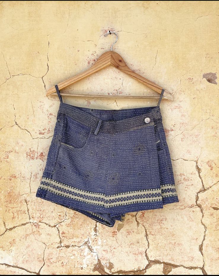 Day and age Blue skorts with white embroidery on a wooden hanger against a textured beige wall. By two extra lives