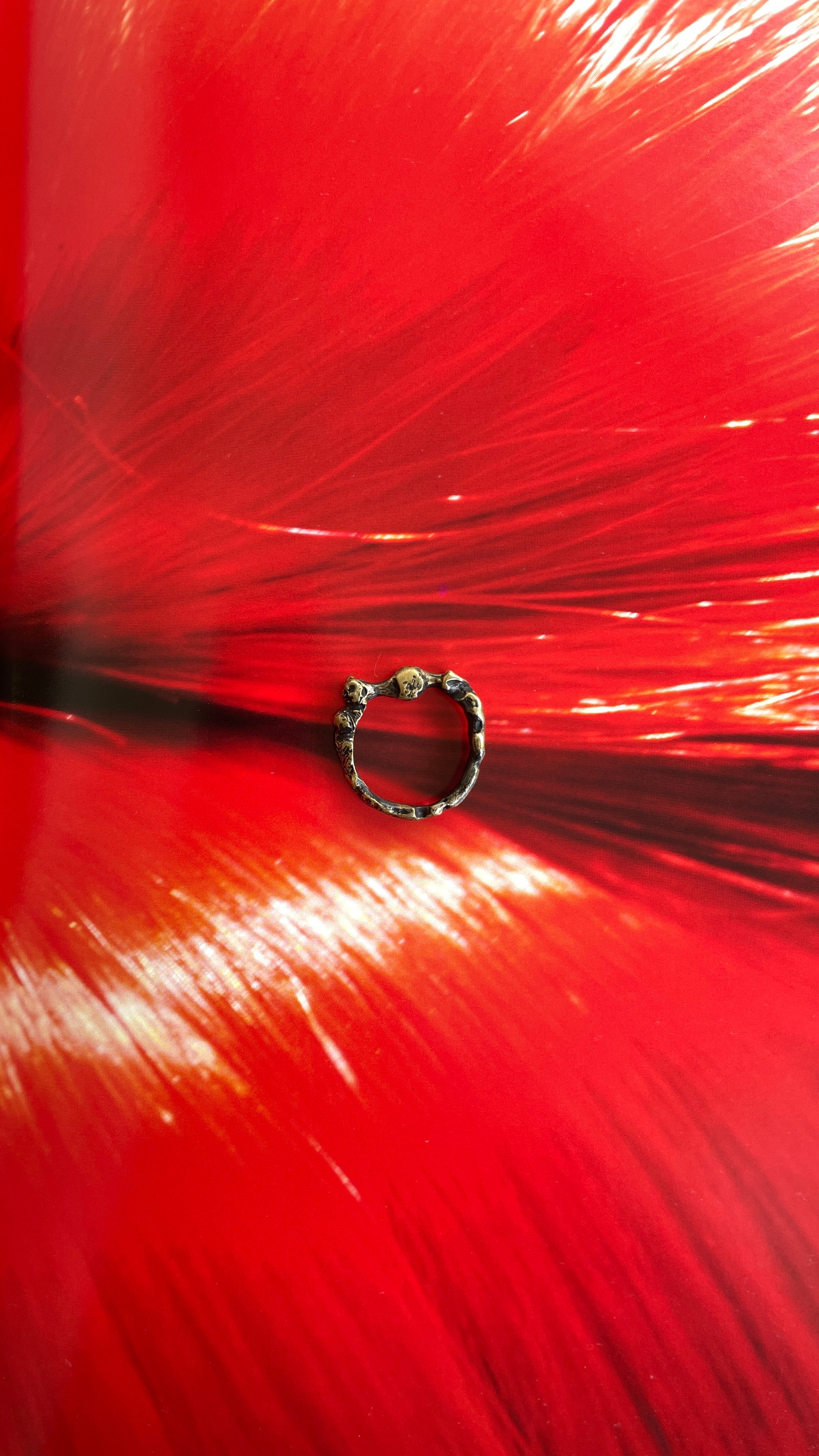 A close-up image of a red textured surface with a circular ring in the center, against which the background is slightly blurred. Ex Nihilo - Atlas Ring sold by two extra lives