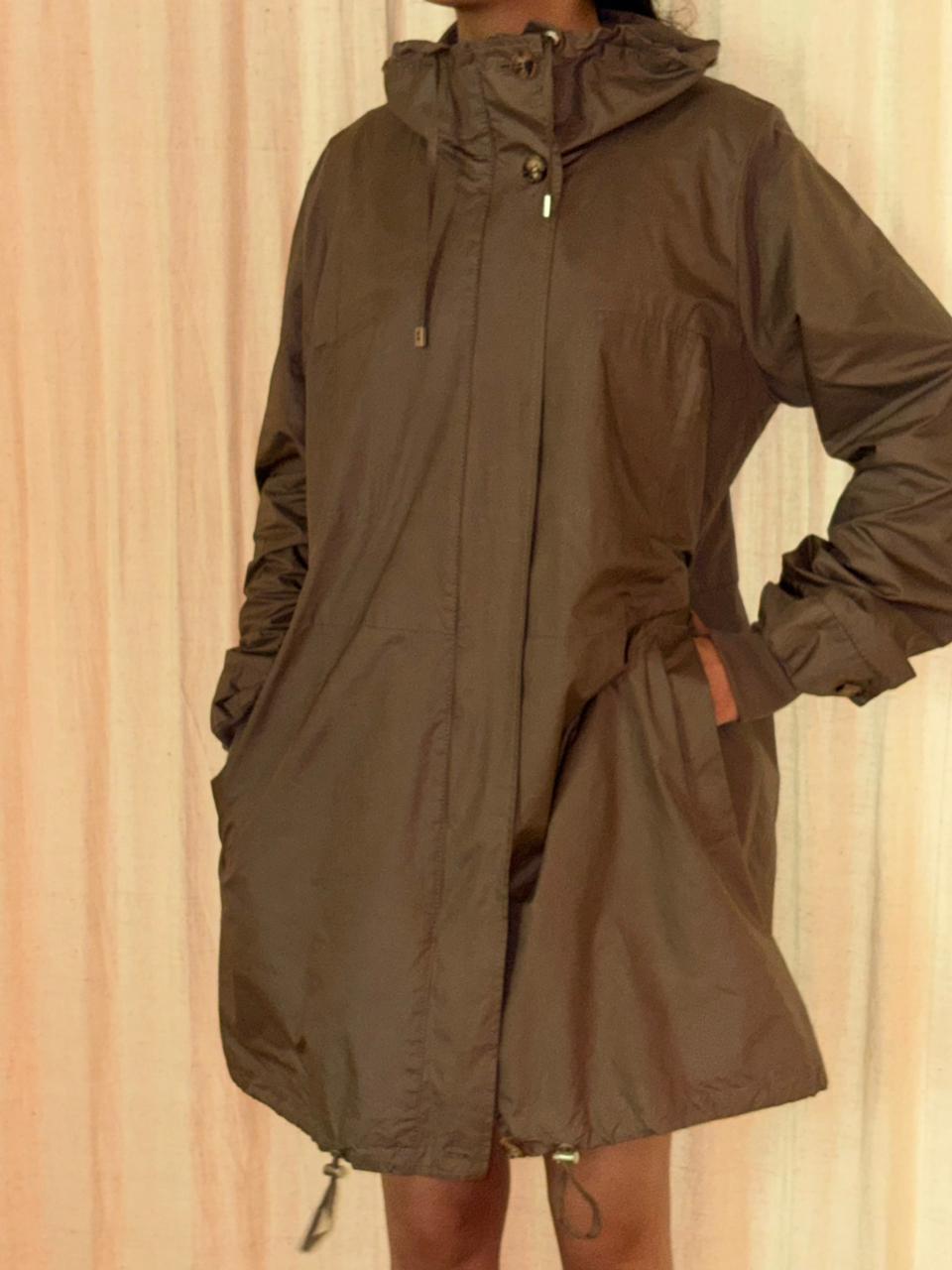 Person wearing a brown raincoat against a beige curtain background FROM-THE-MIND-UPCYCLED-VOYAGE-JACKET