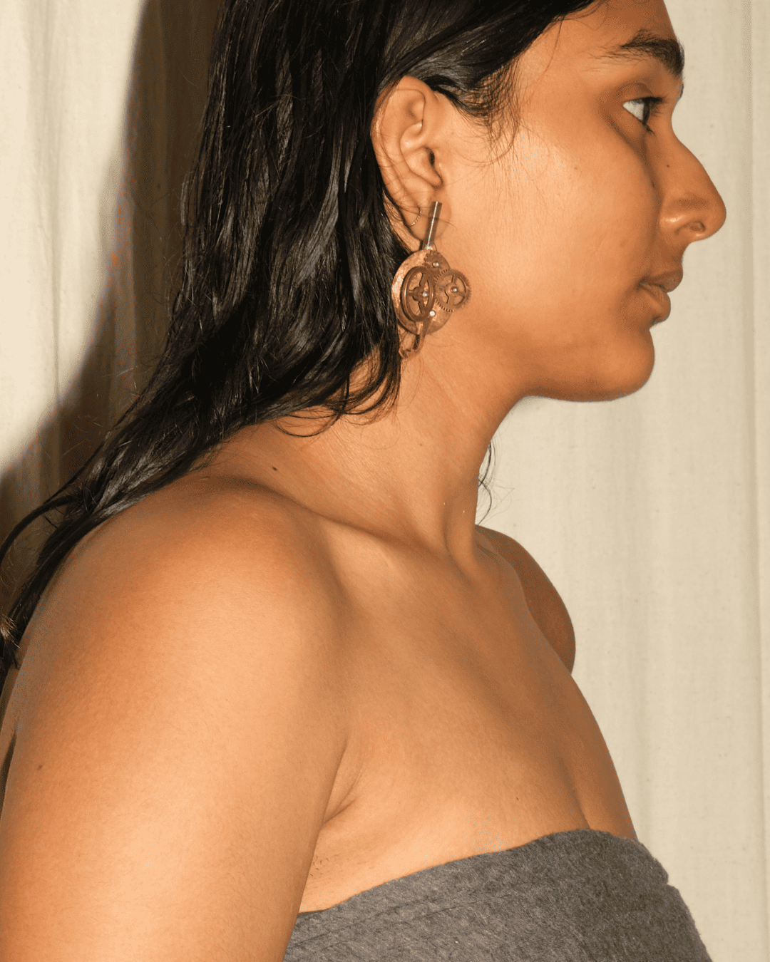 A woman shown in side profile wearing a large, sculptural, translucent amber-brown glass earring with a dark metal top hook.