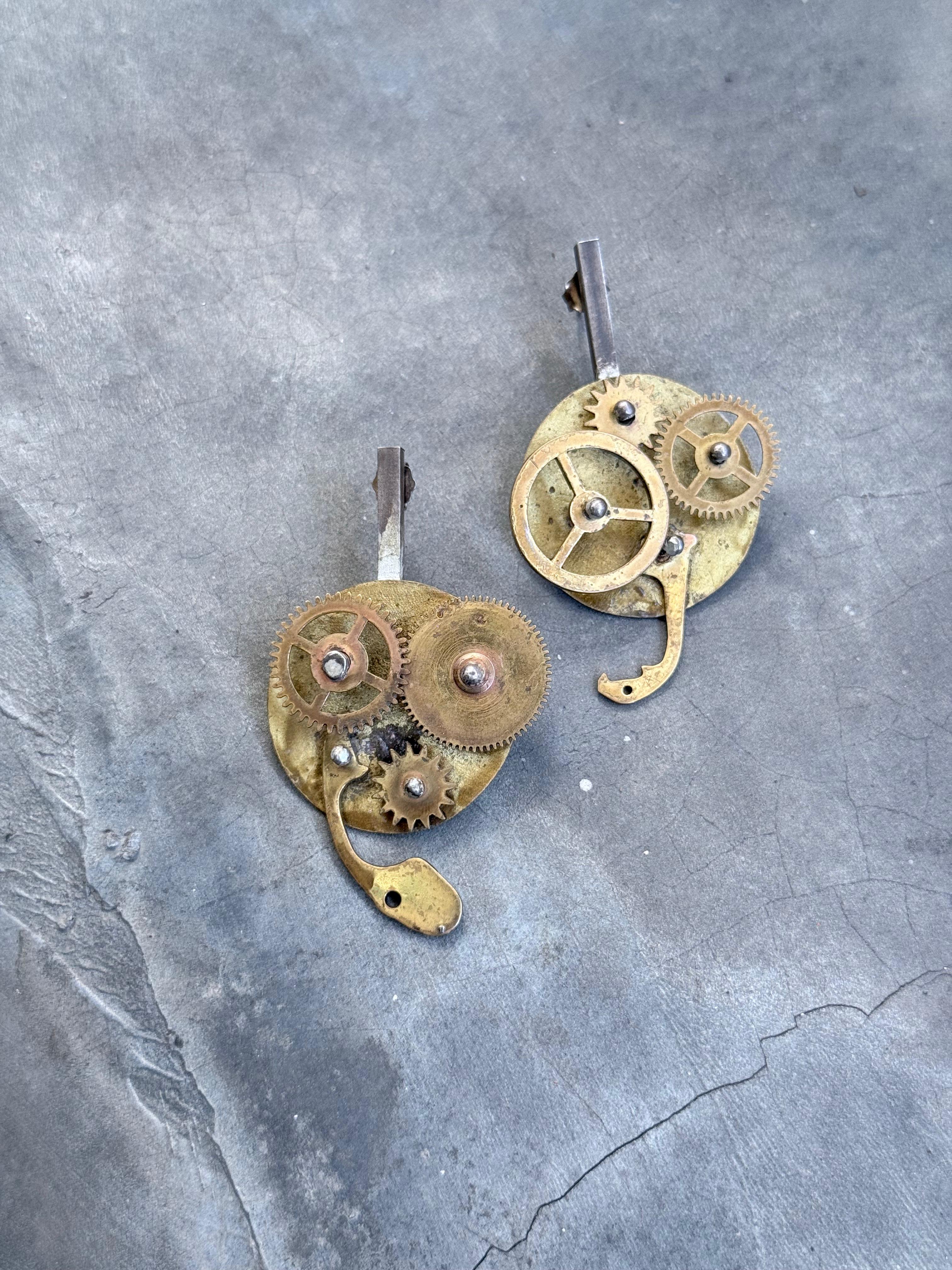 A pair of earrings crafted from metal gears, displayed against a textured background.