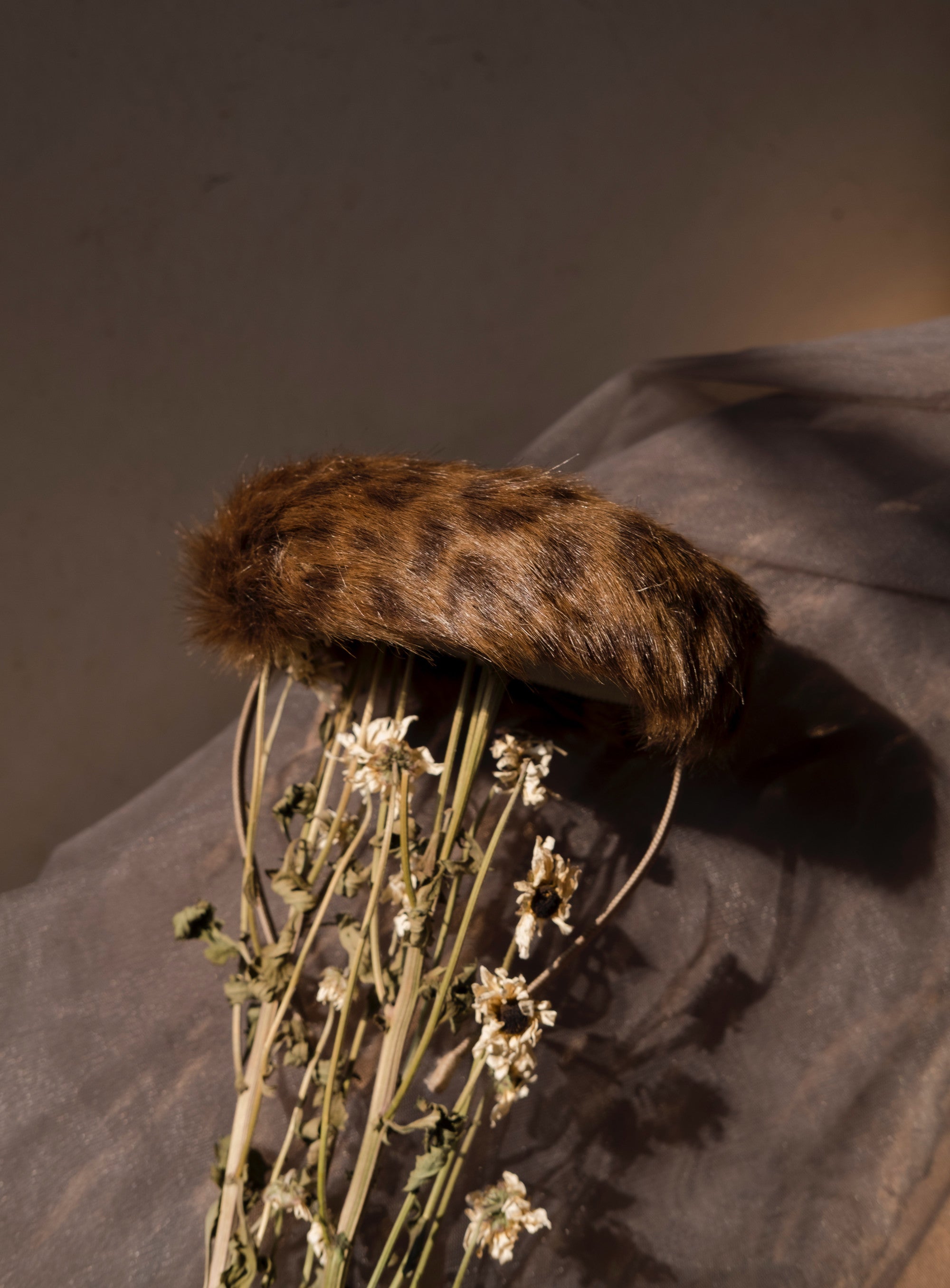 A faux fur hat in a cheetah print, styled on a mannequin with a backdrop of dried flower stems. Kitty Comet - Cheetah Print Fury Hat sold by two extra lives