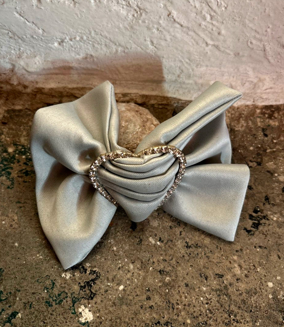A silver-colored bow-shaped ring on a textured surface. Merrfer - Bow Ring sold by two extra lives.