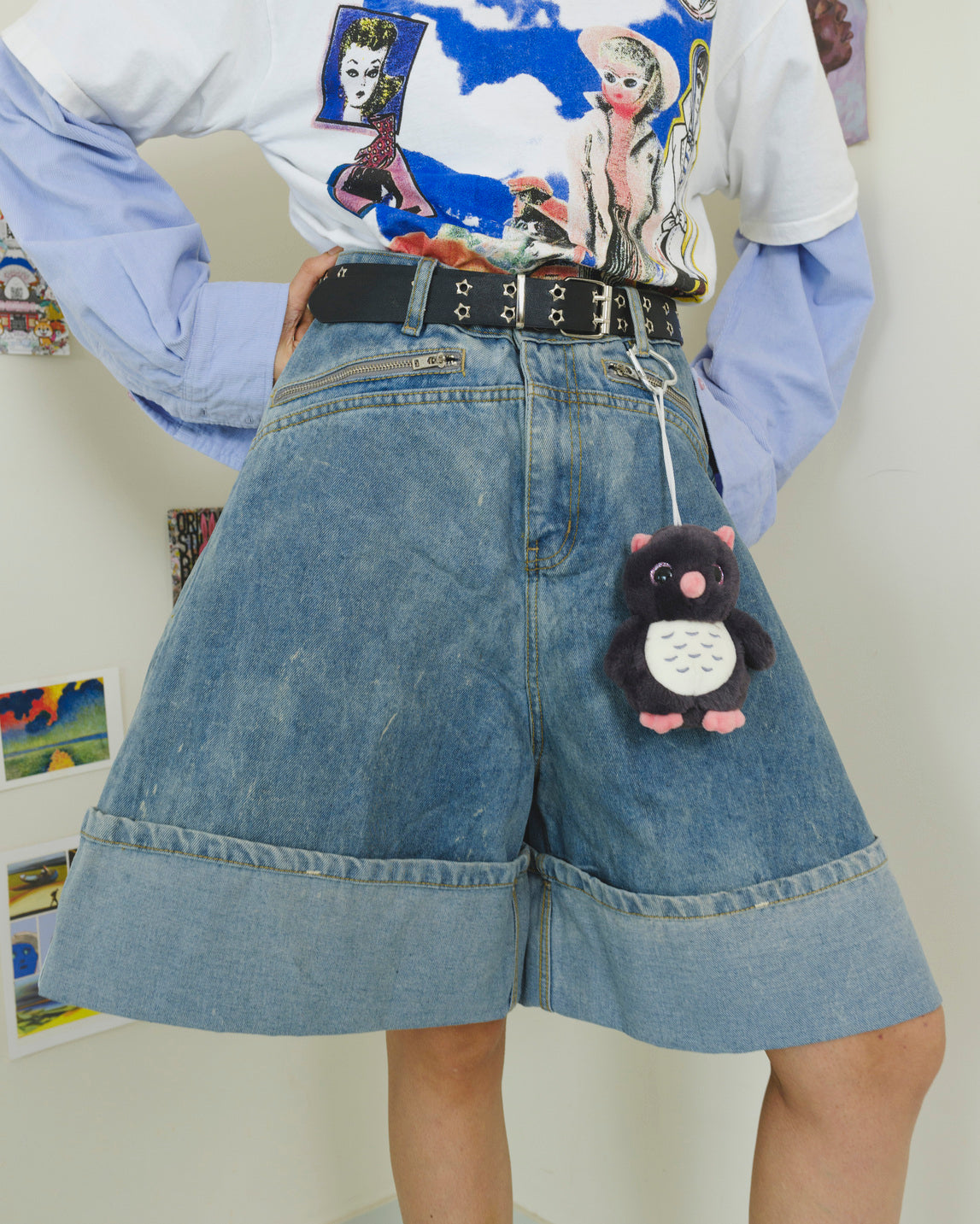 Person wearing a graphic t-shirt, denim shorts, and a keychain with a cartoon character.