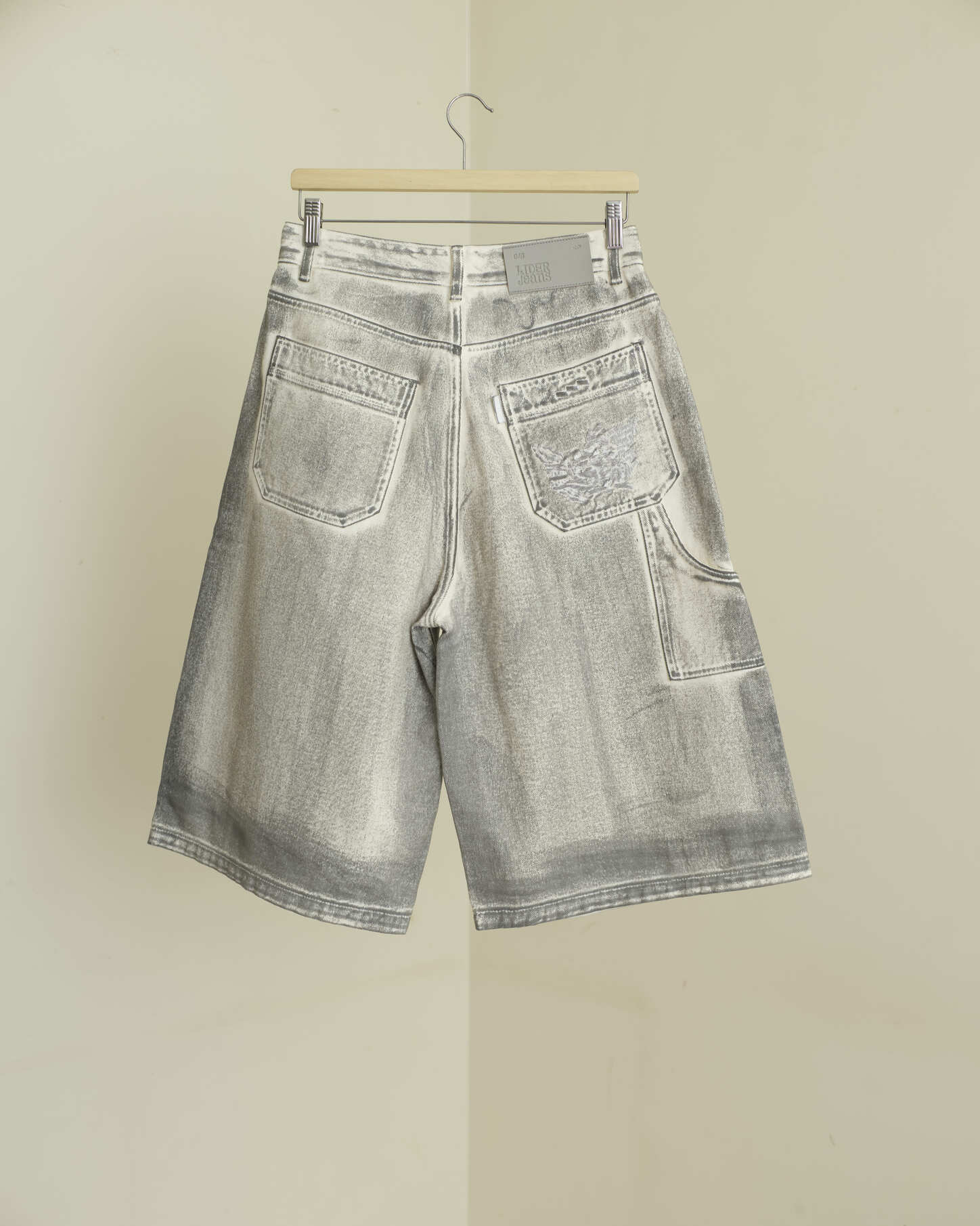 Gray denim shorts on a hanger against a beige wall