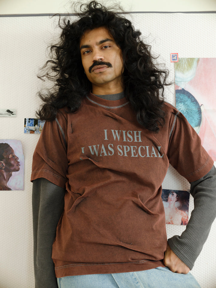 Person wearing a brown sweatshirt with text, standing against a wall with posters.