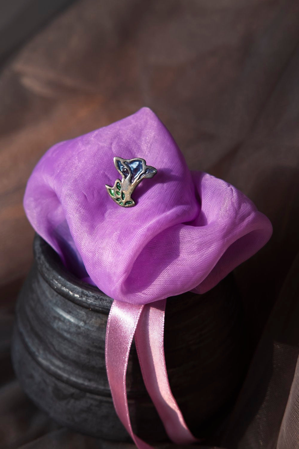 A pair of silver earrings designed in the shape of a Morning Glory flower, displayed on a purple fabric, placed on the edge of a black pot. Peca Joyería Poética - Morning Glory earring sold by two extra lives