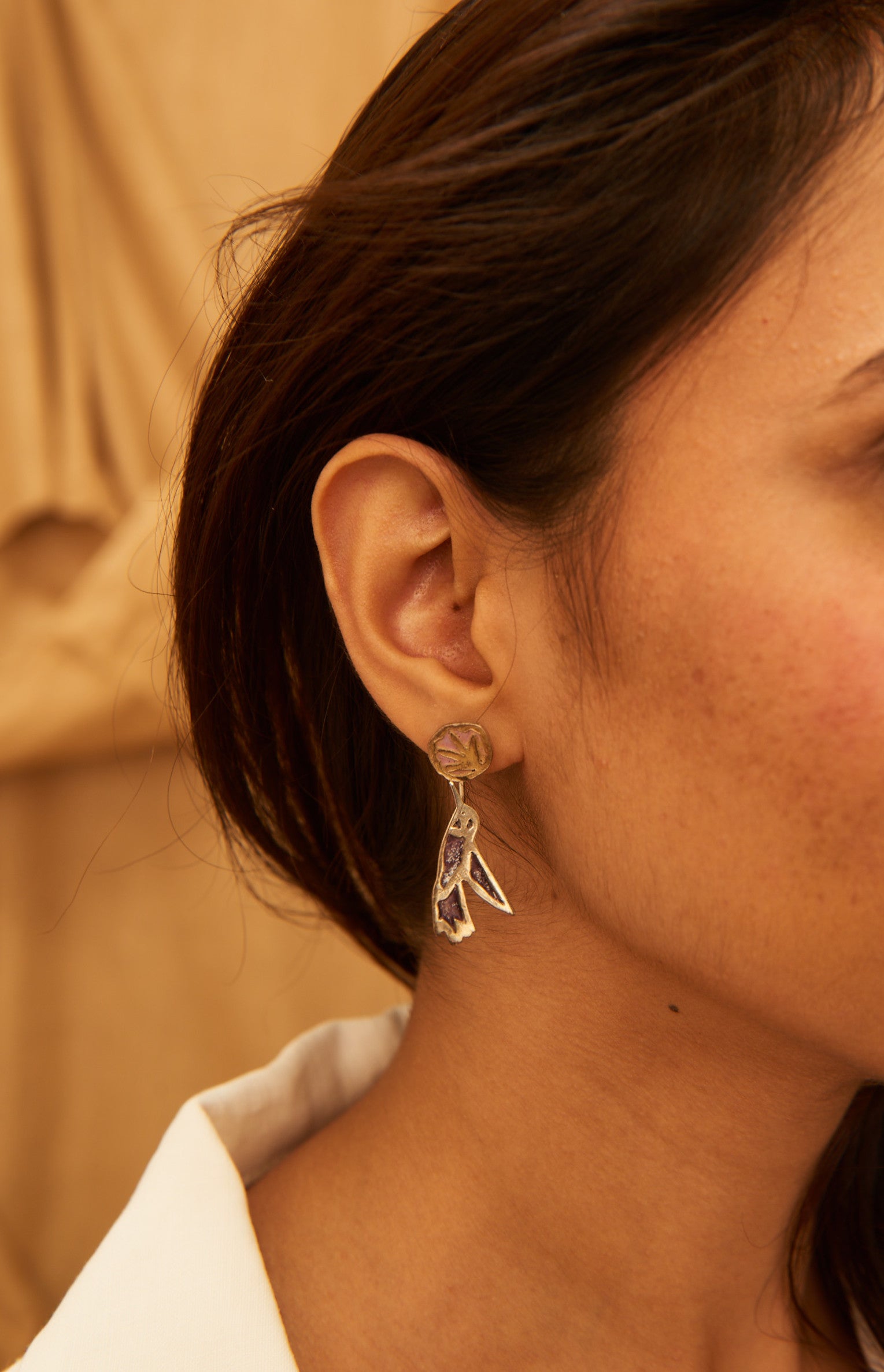 A pair of silver earrings with an abstract design, displayed inside a textured, black earring holder. 
Peca Joyería Poética - Swallow Earring sold by two extra lives