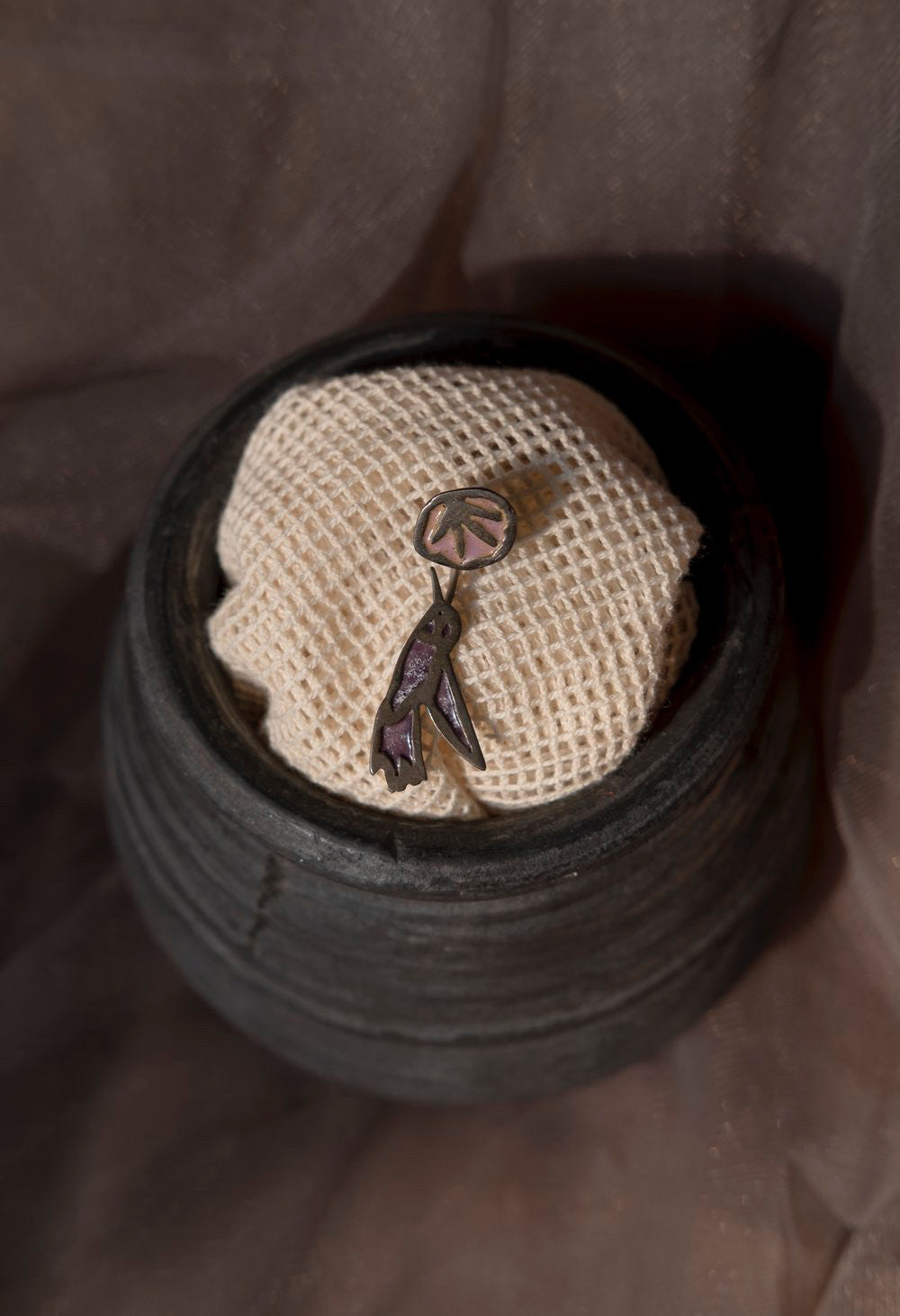 A pair of silver earrings with an abstract design, displayed inside a textured, black earring holder. 
Peca Joyería Poética - Swallow Earring sold by two extra lives