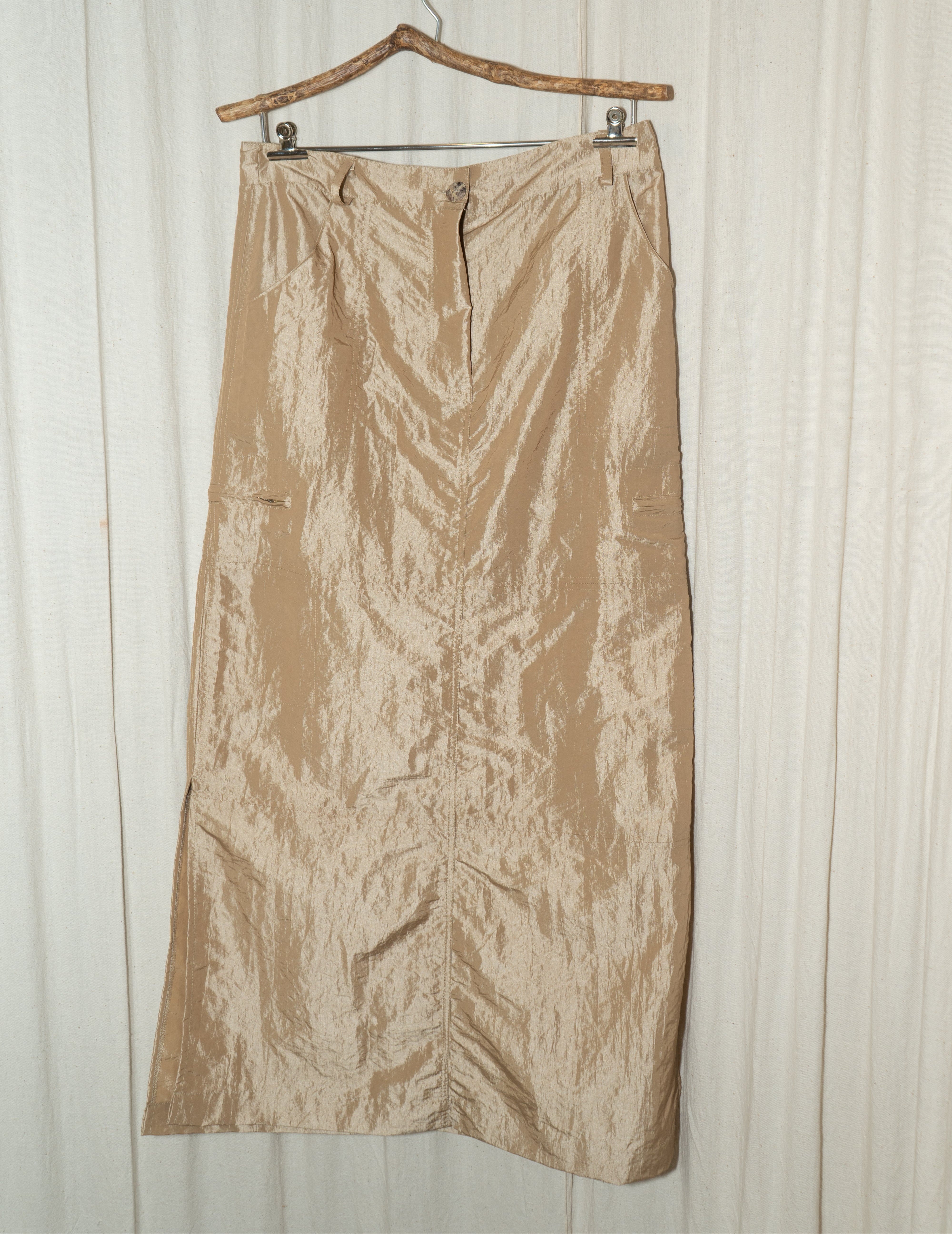 A long, shiny golden skirt with side slits, button detailing, and belt loops, featuring a zippered closure at the back.