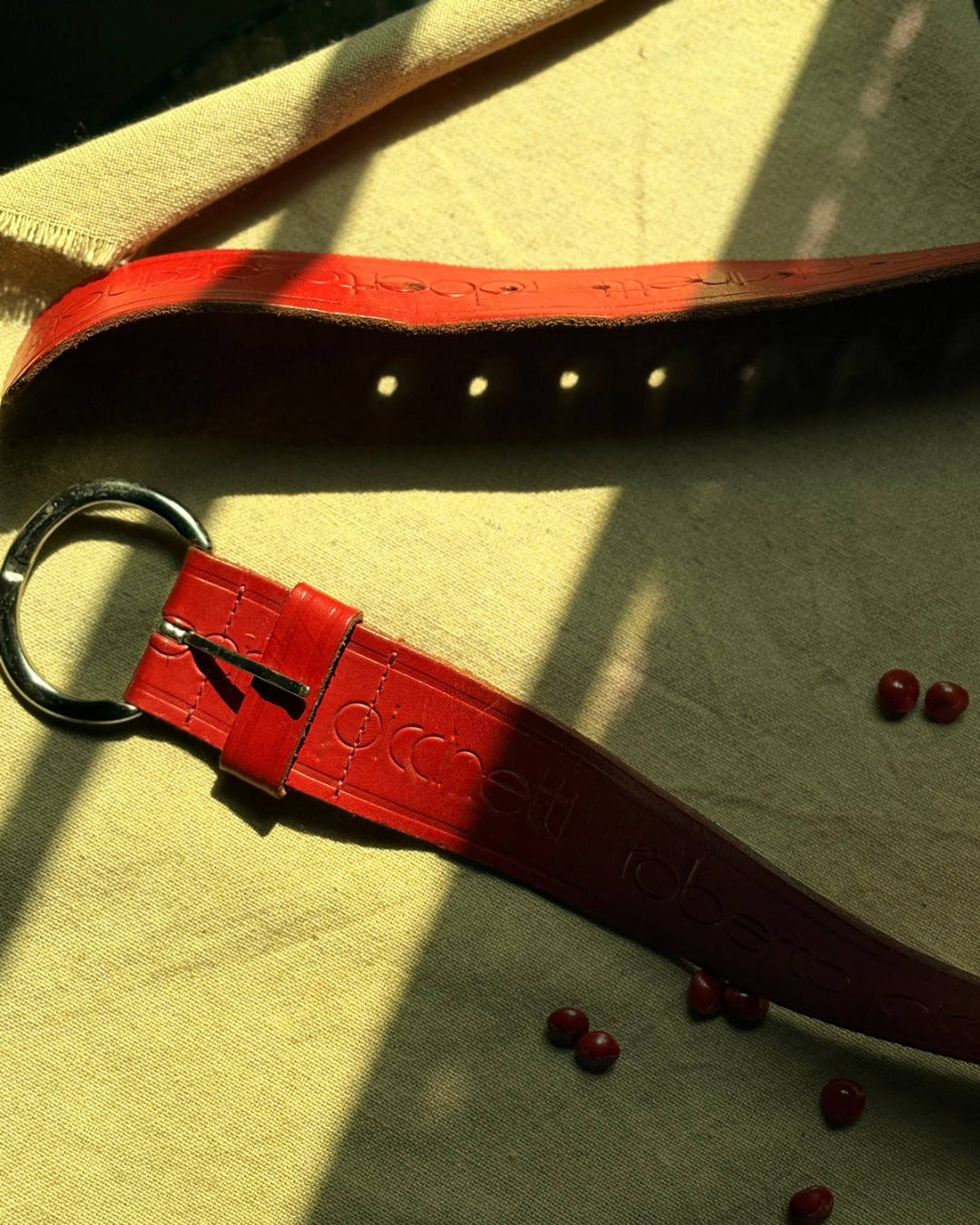 Red leather belt with a keychain on a textured surface sold by two extra lives