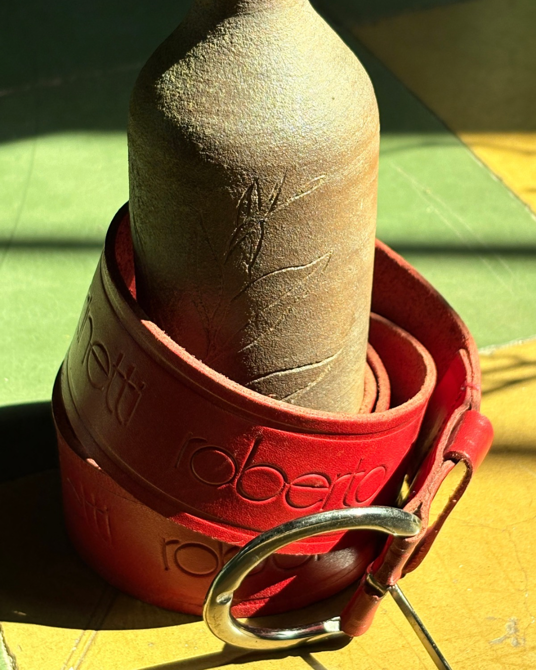 Red belt with a textured brown bottle on a green and yellow surface Roberto-Pinccinetti-Red-Belt-two-extra-lives