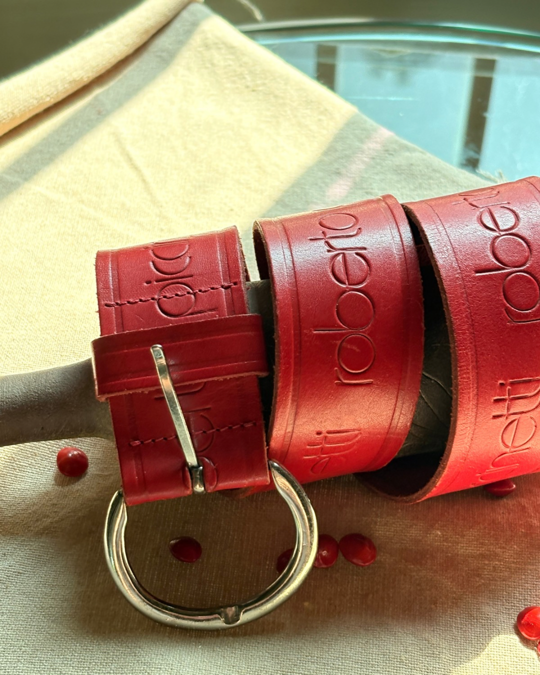 Red belt with 'Dolci Roberto' branding on a fabric surface. Roberto Pinccinetti Red Belt two extra lives