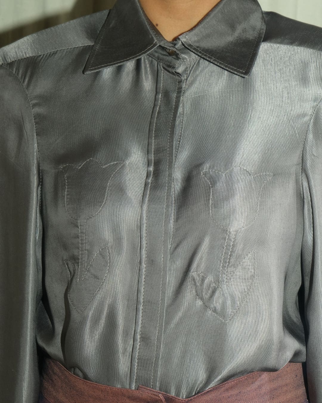 Close-up of a gray satin-like collared blouse with tonal embroidered floral motifs on the front, worn with a dusty rose skirt.