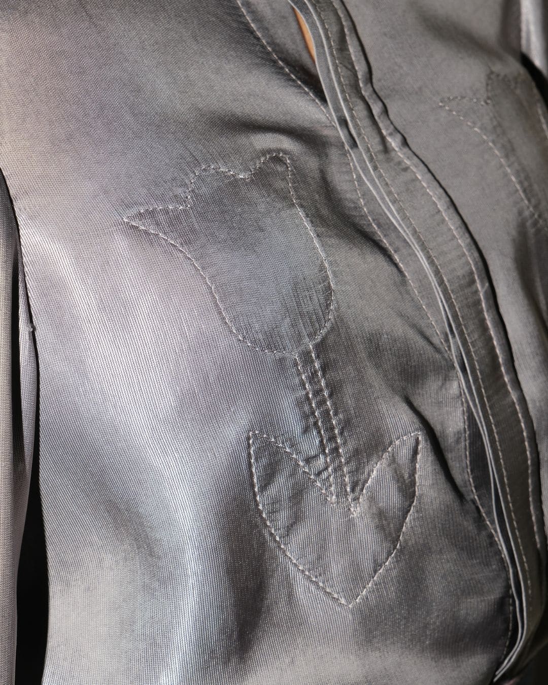 Close-up of a gray satin blouse featuring a large embroidered tulip motif on the front.