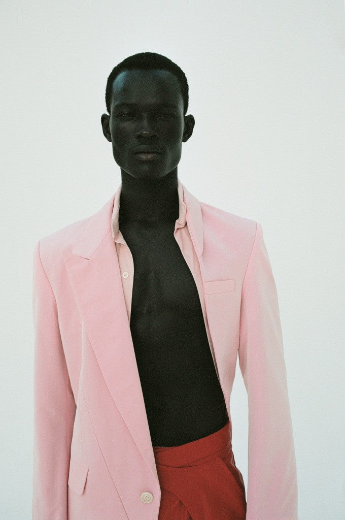 A person wearing a pink asymmetrical jacket and red trousers, with their face partially obscured by the jacket.