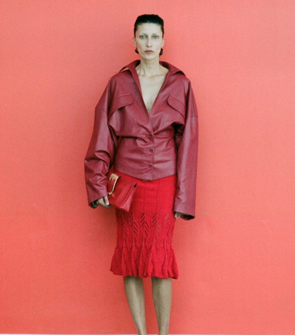 Woman wearing a red leather jacket and skirt against a pink background