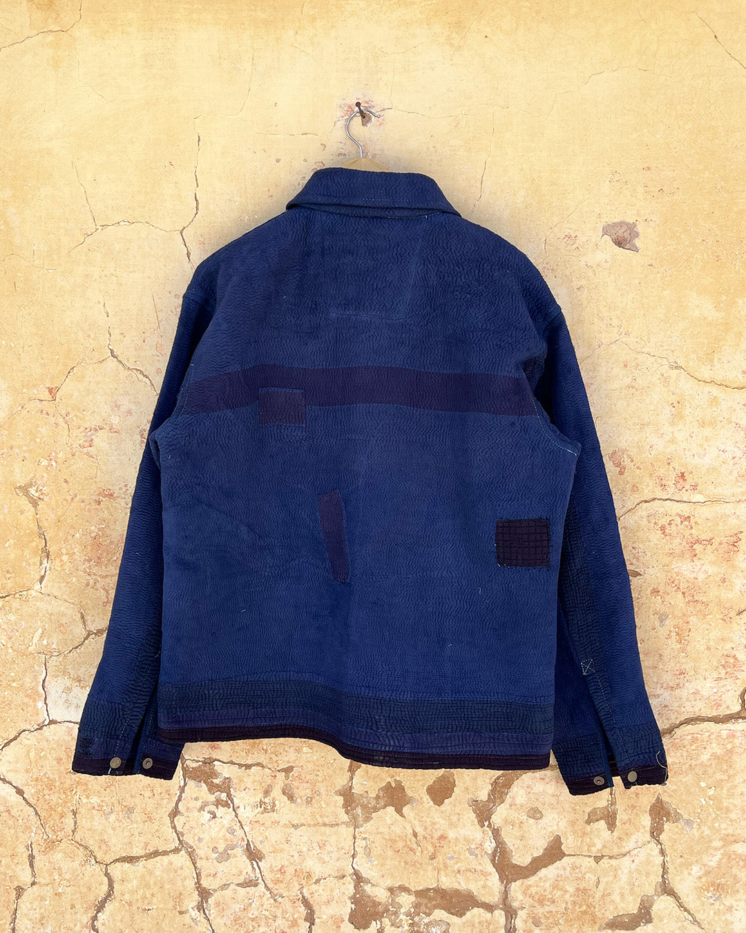 Blue jacket hanging on a textured beige wall day-and-age-marina-jacket-two-extra-lives