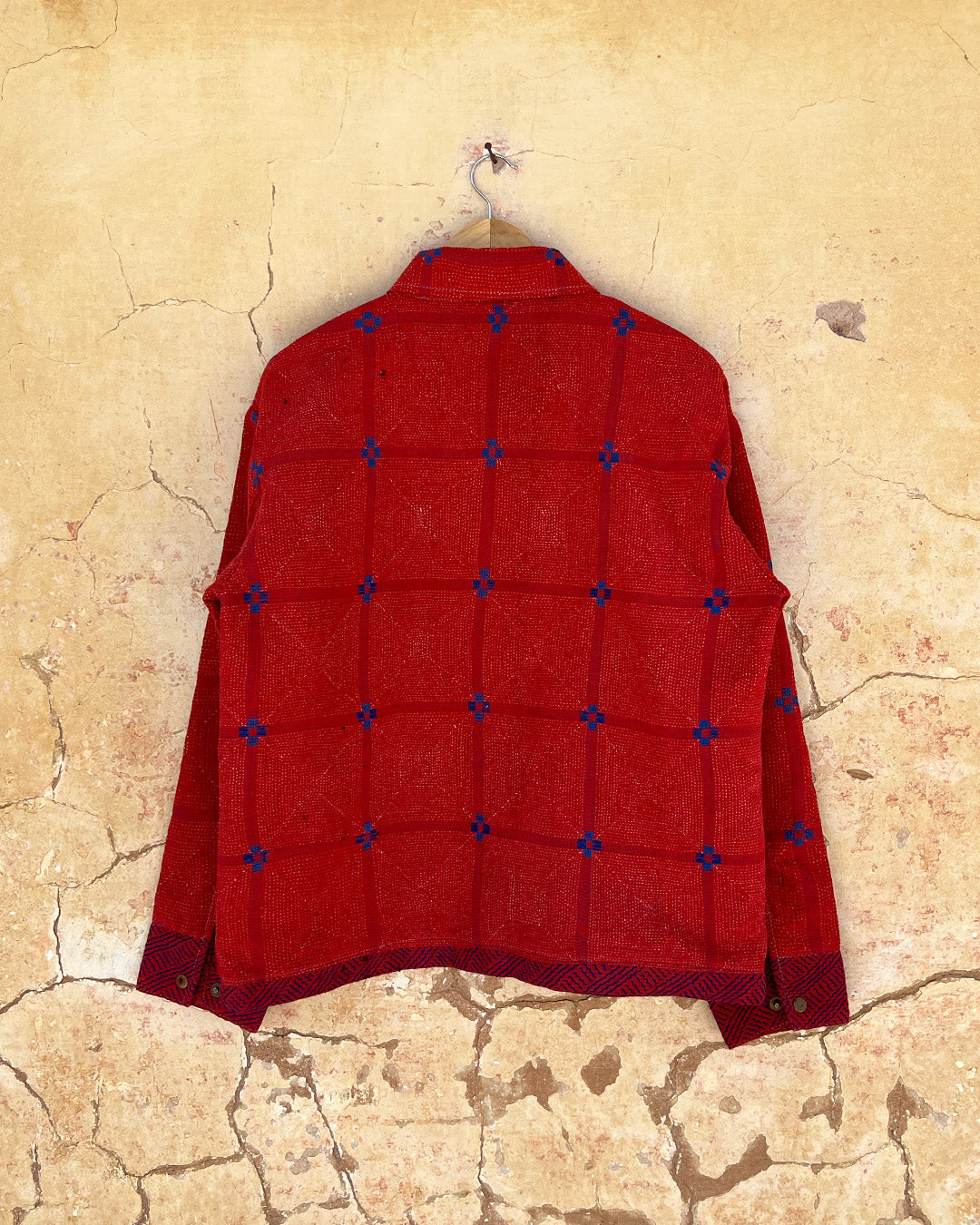 Red quilted jacket with blue accents on a beige textured wall day-and-age-steaam-angine-jacket-two-extra-lives