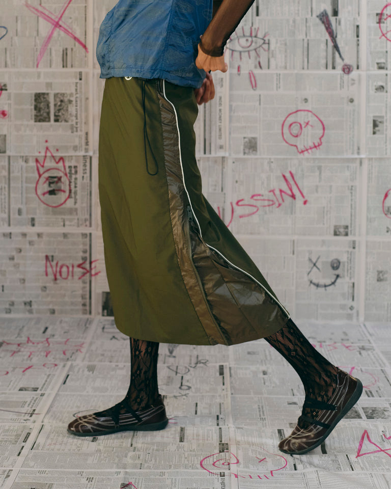 Person wearing green pants with a white stripe, standing on a floor with graffiti.